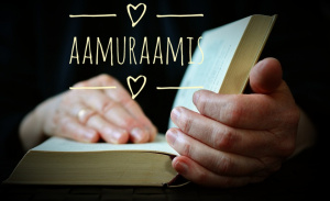 Kuvan etualalla kädet, jotka selaavat Raamattua. Kuvan tausta on tumma. Kuvassa lukee teksti Aamuraamis.  Kuva on 